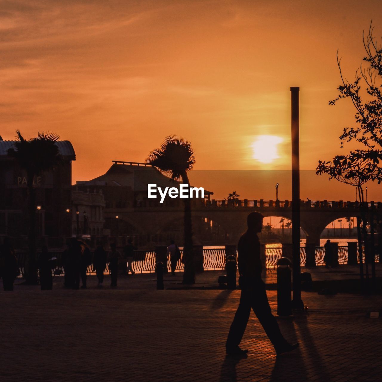 SILHOUETTE WOMAN WALKING ON SIDEWALK IN CITY DURING SUNSET