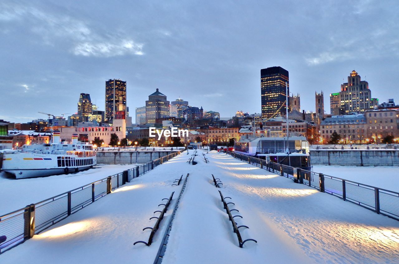 Snow covered bridge in city against sky