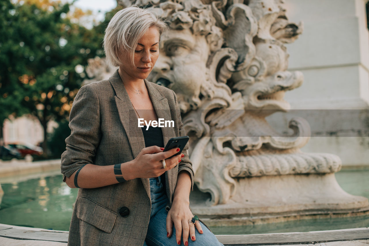 Woman texting in her mobile phone while sitting at fountain