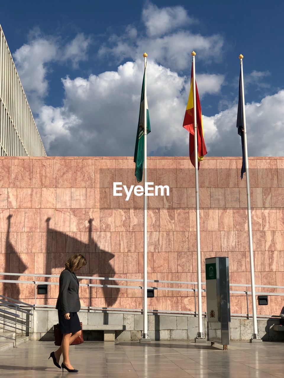 WOMAN STANDING BY FLAGS AGAINST SKY