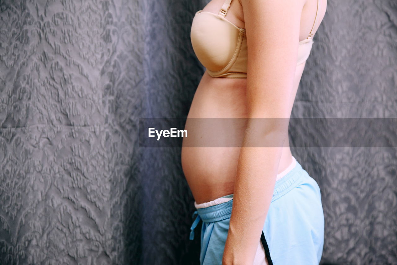 Midsection of pregnant woman standing against curtain