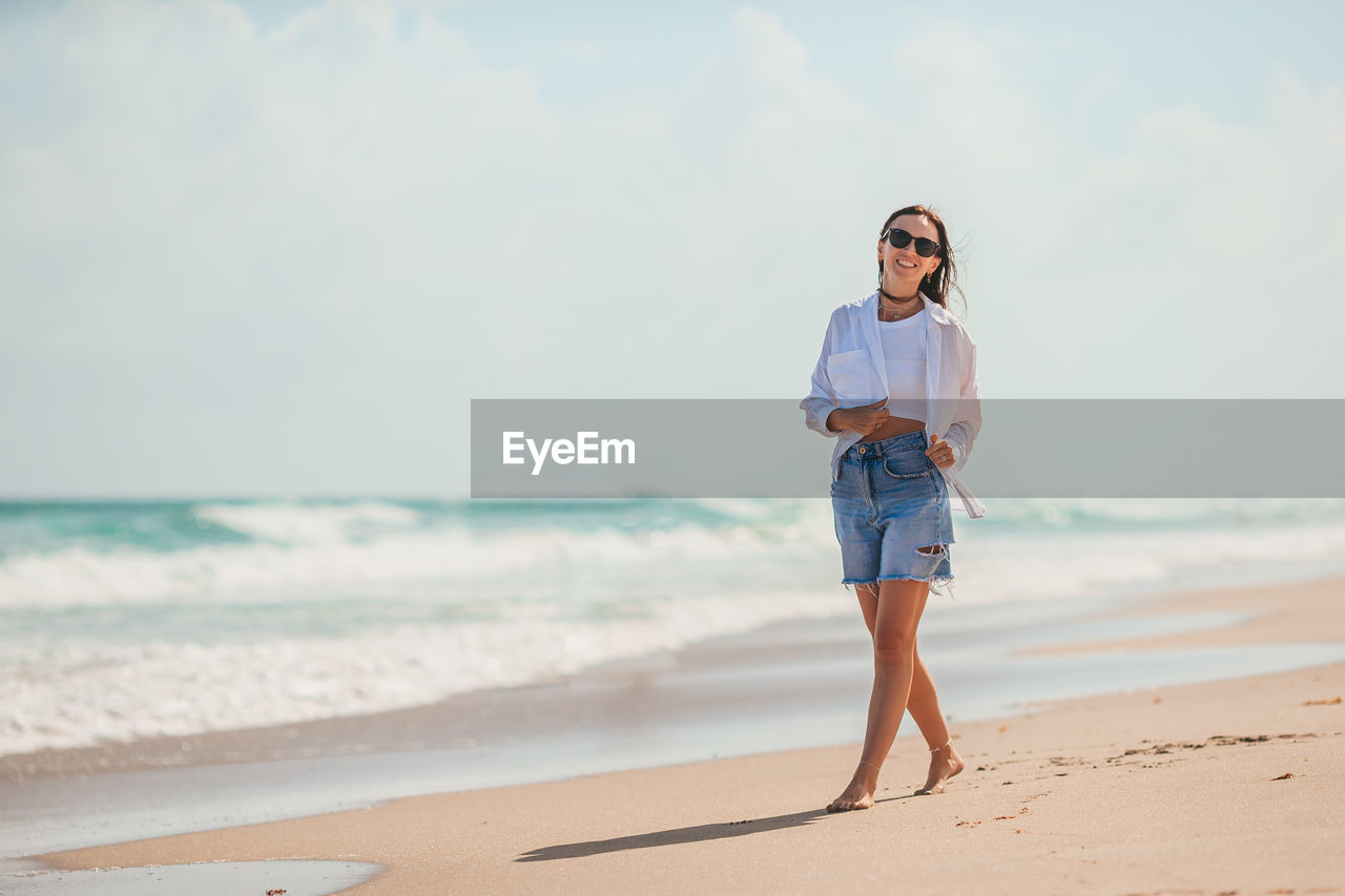 portrait of young woman standing at beach against sky