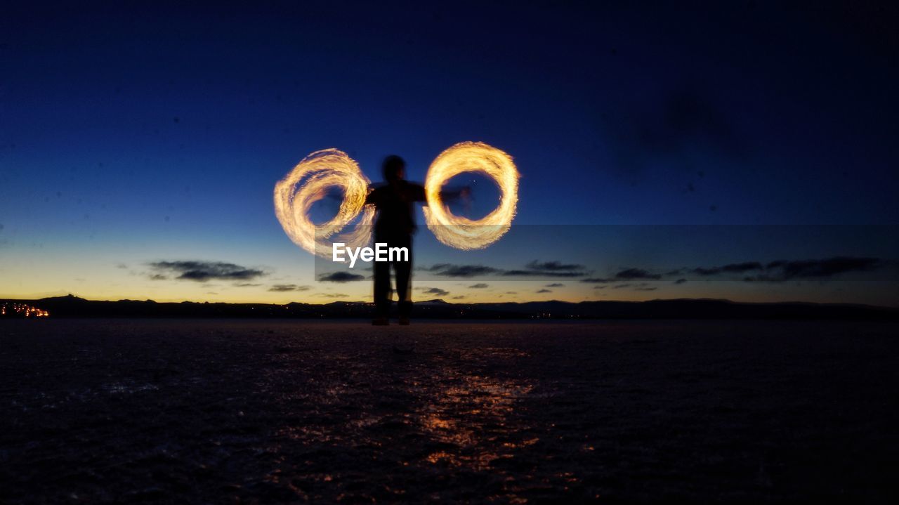 Man spinning wire wool on field against sky at night