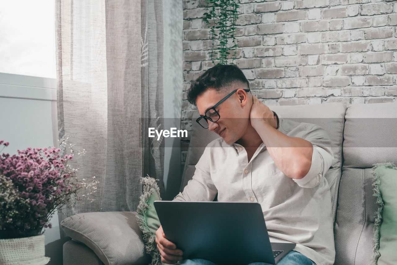 young man using laptop while sitting against wall