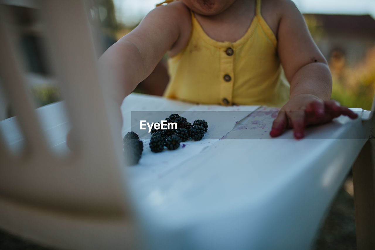 Midsection of baby girl with blackberries on table