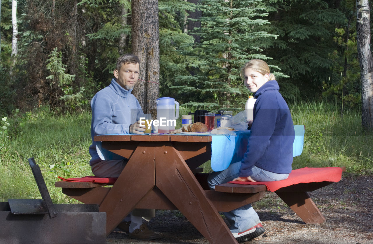 Portrait of father and daughter having food and drink on picnic table in forest