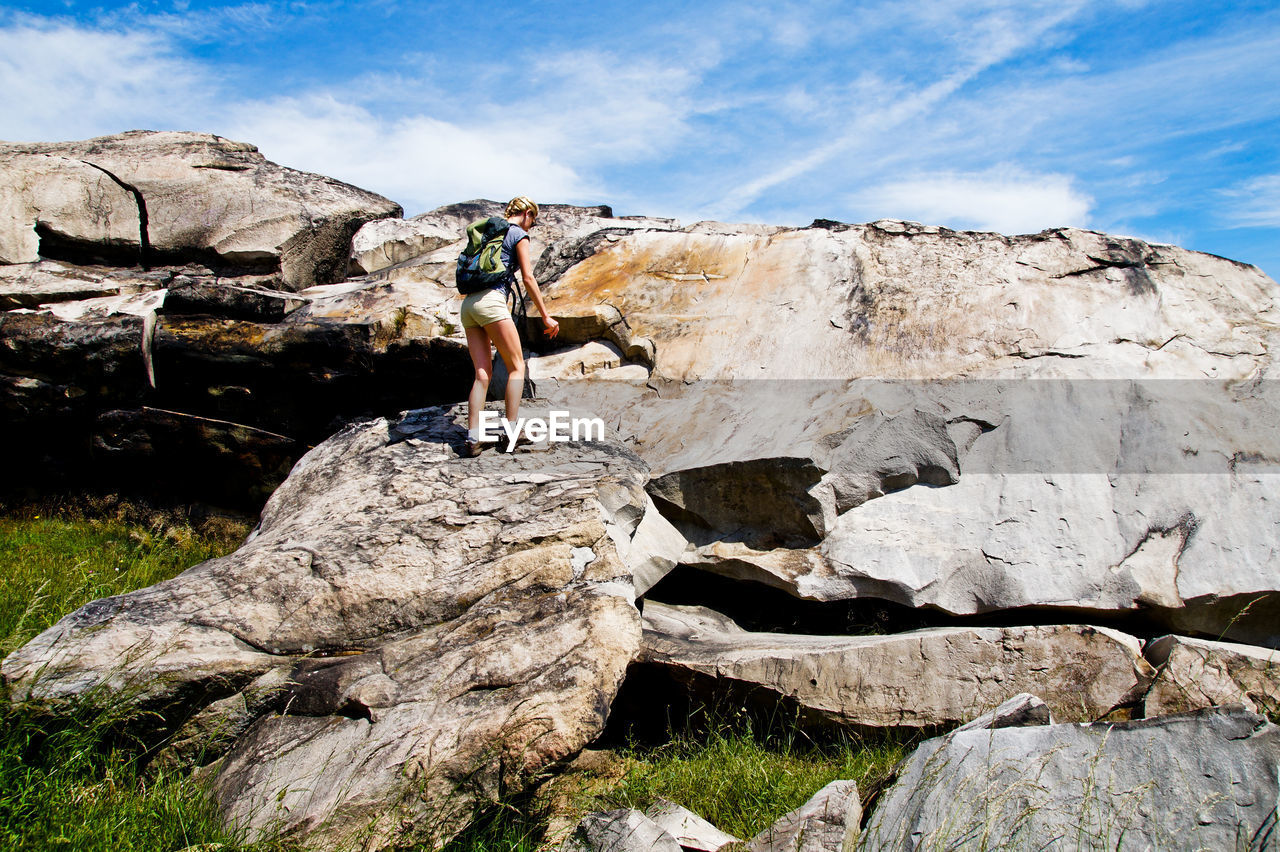Female hiker standing on rock formation against sky during sunny day