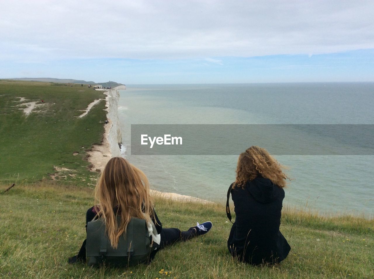 Rear view of women sitting on grass at seven sisters while looking at horizon