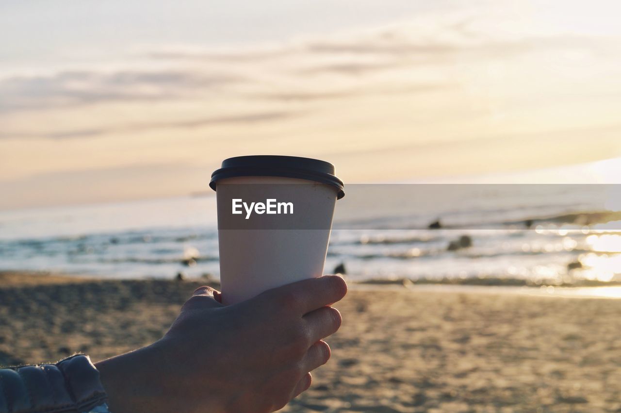 CLOSE-UP OF HAND HOLDING DRINK AT BEACH