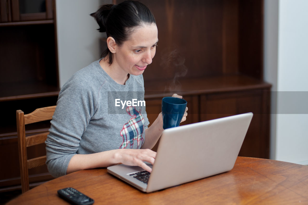 Woman having coffee while using laptop on table