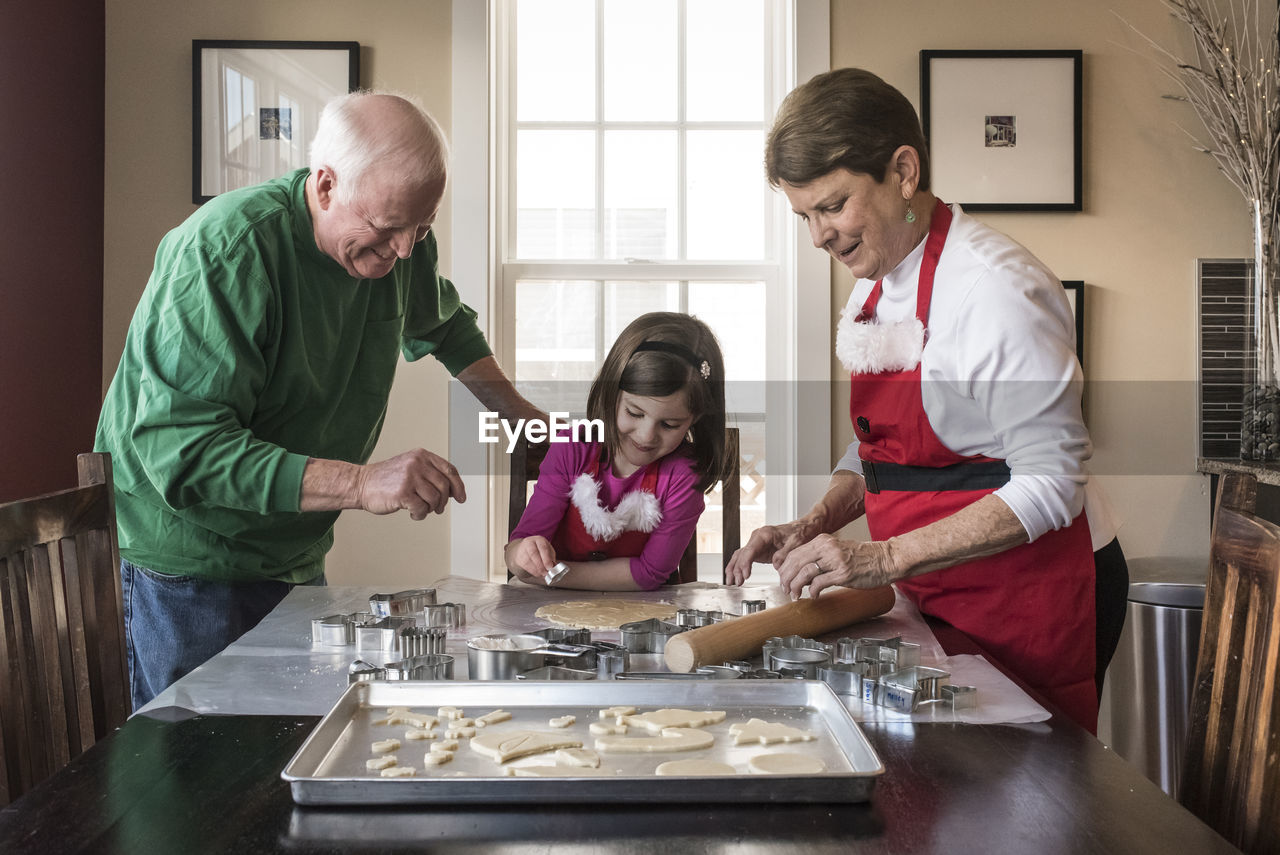 Cute granddaughter making gingerbread cookies with grandparents at home