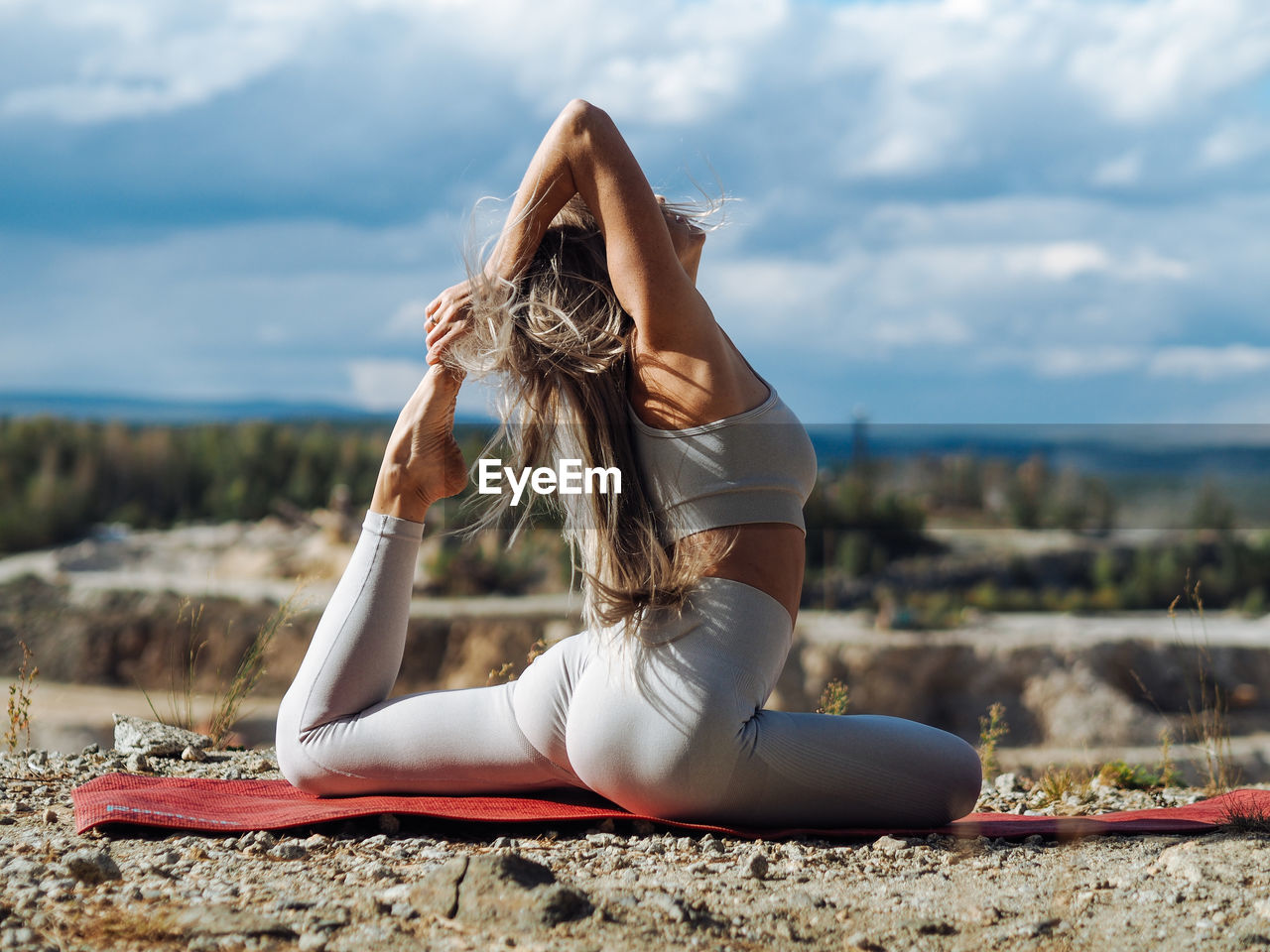 Young beautiful blond woman with long hair in activewear doing yoga pose in outdoor training in hill