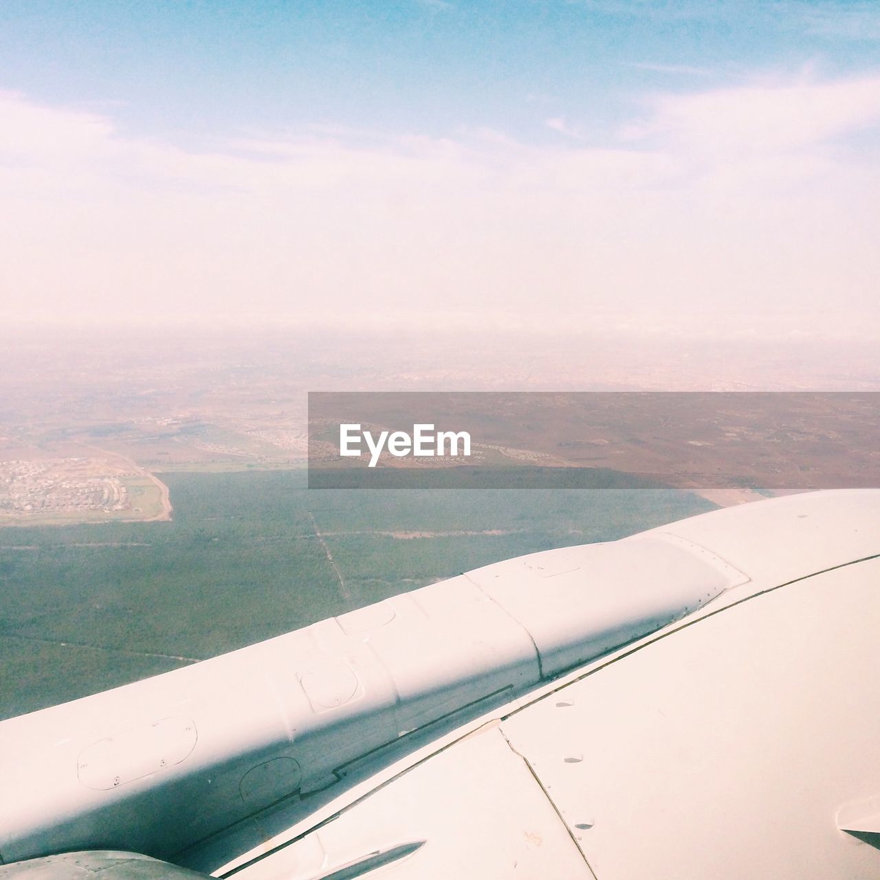 Cropped image of airplane flying over landscape against sky