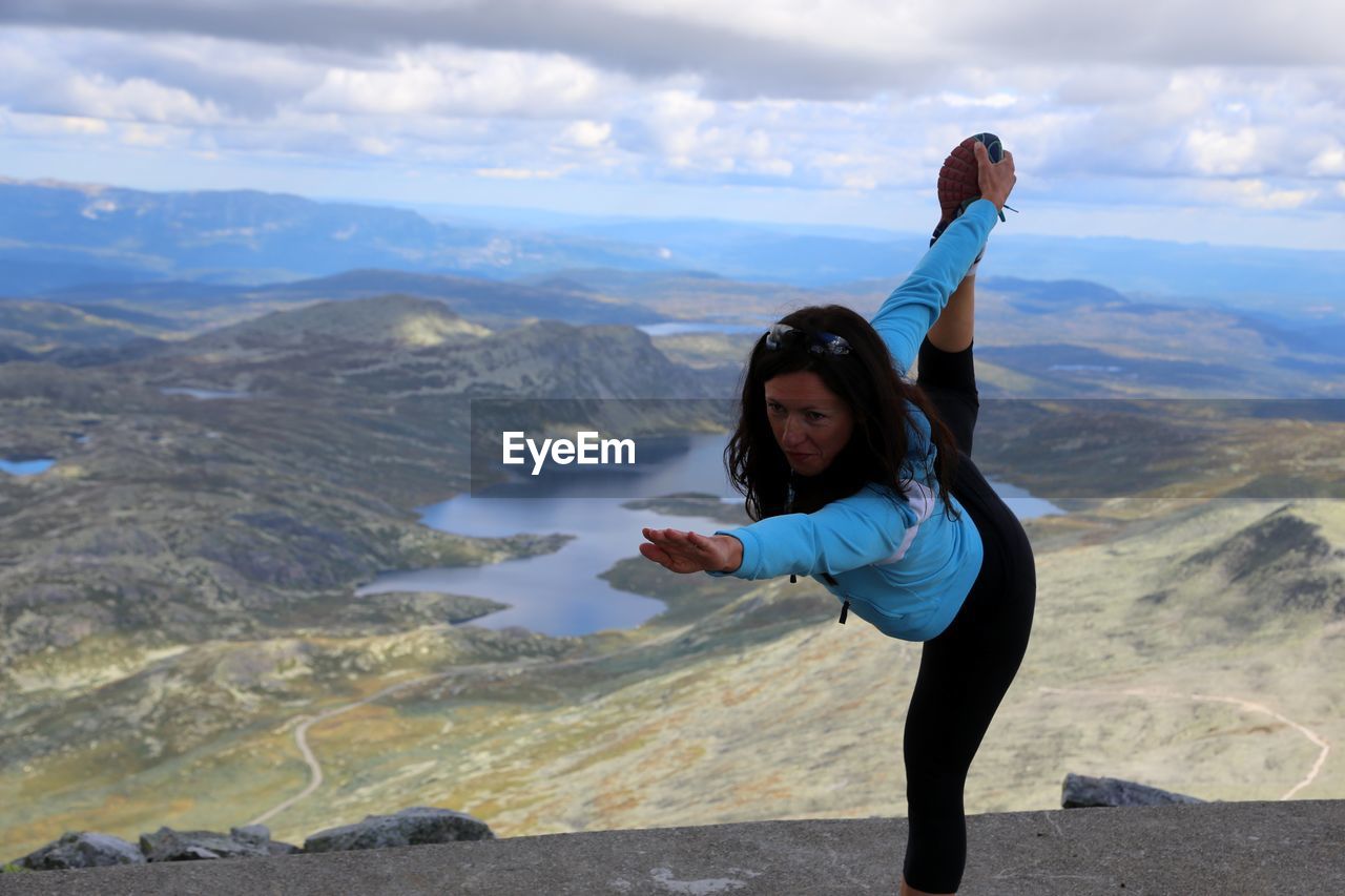 YOUNG WOMAN LOOKING AT SEA AGAINST MOUNTAIN