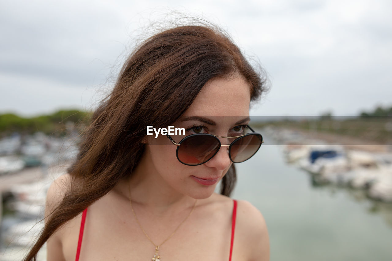 Close-up of thoughtful woman wearing sunglasses while standing against harbor