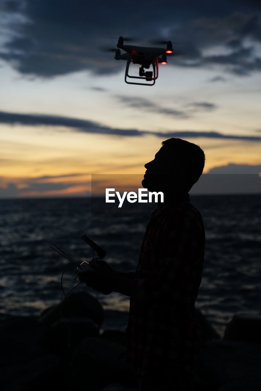 Silhouette man photographing sea against sky during sunset