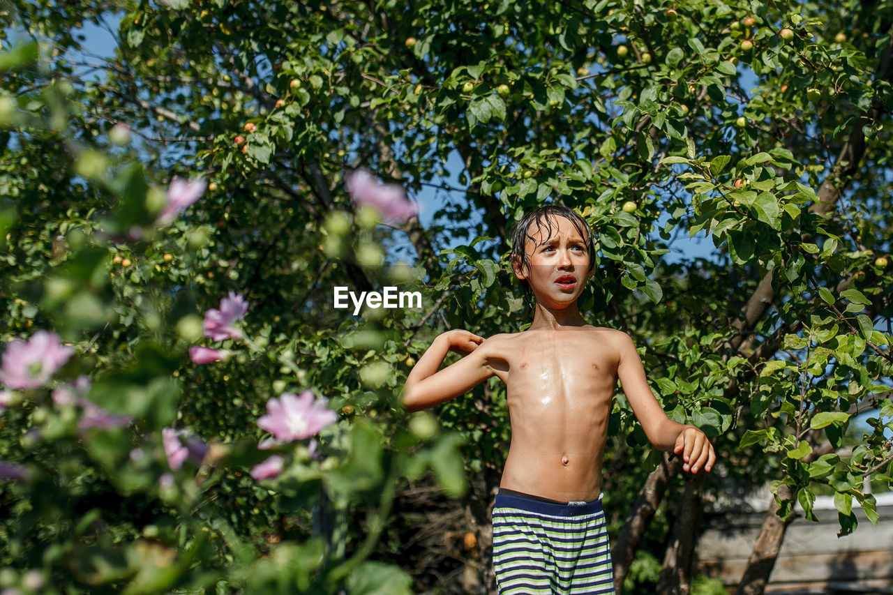 Shirtless boy standing against tree