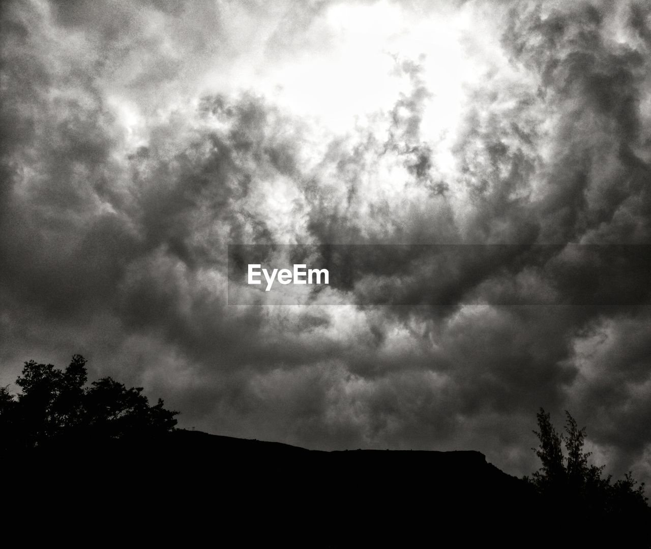 SILHOUETTE OF TREES AND MOUNTAINS AGAINST CLOUDY SKY