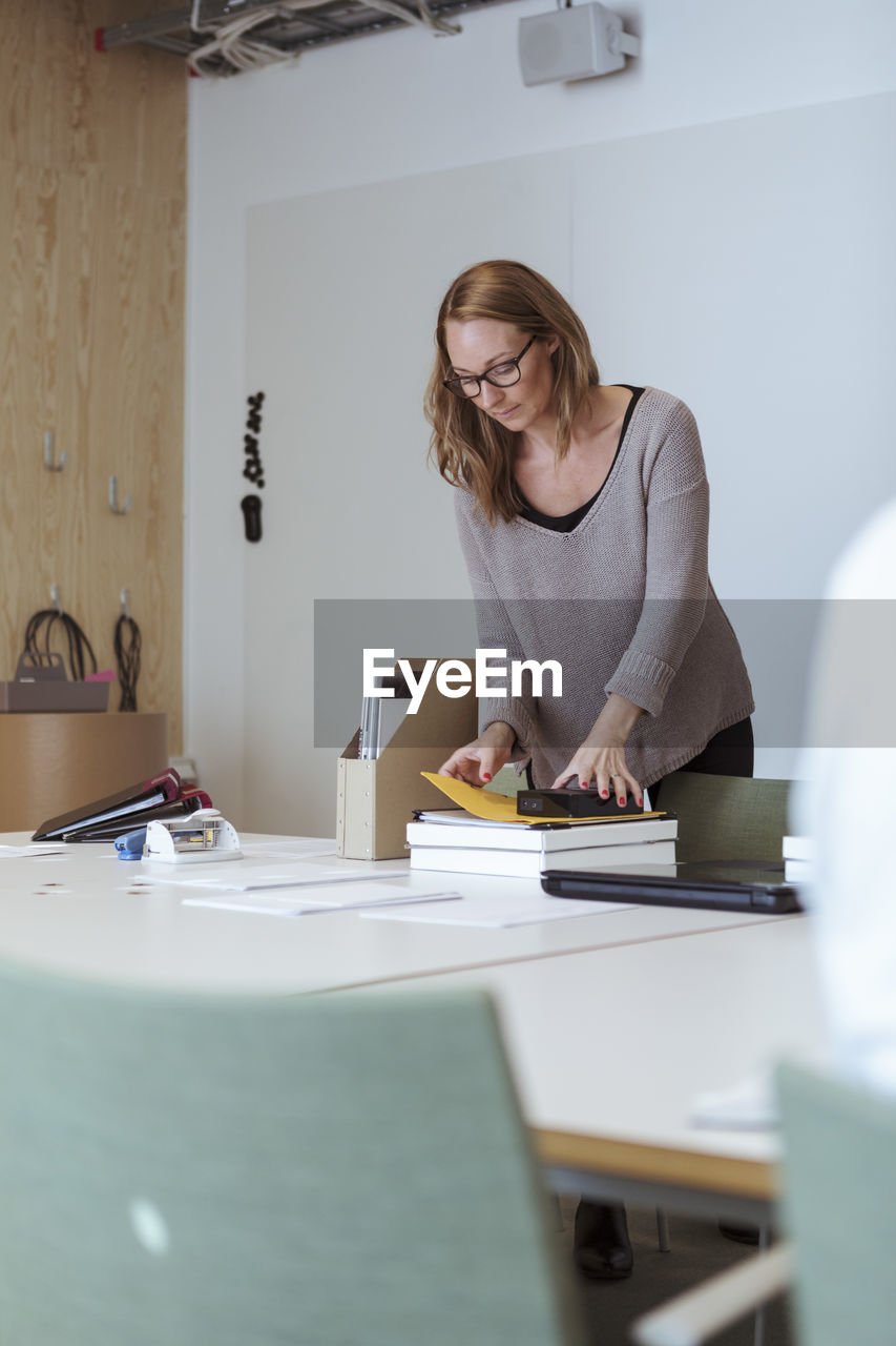 Mid adult female executive examining files on conference table at office