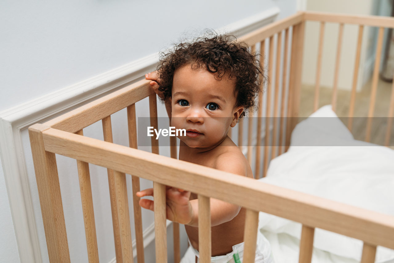High angle portrait of cute shirtless baby boy standing in crib at home