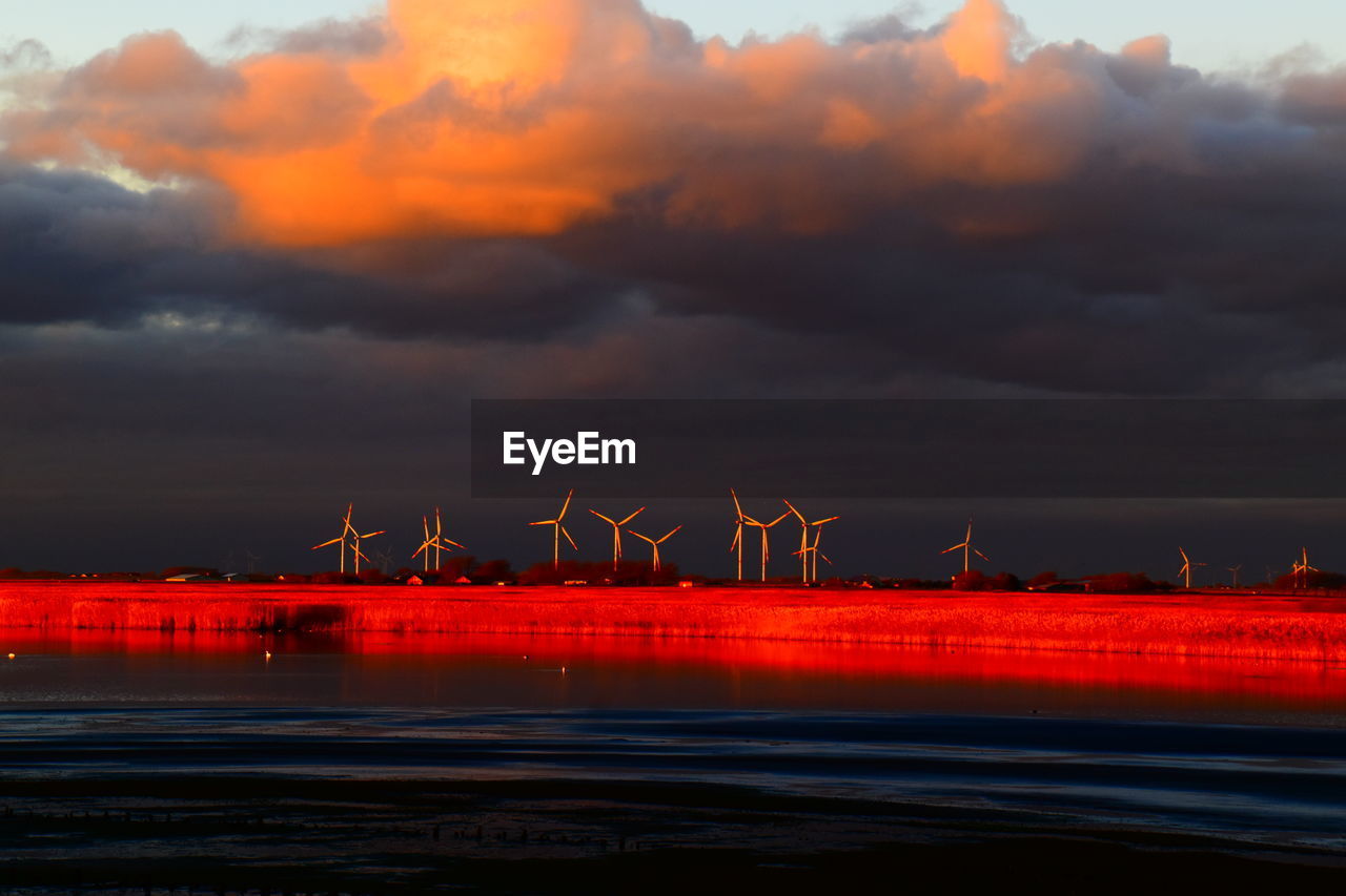 Scenic view of sea against sky during sunset and white windmills on the horizon.