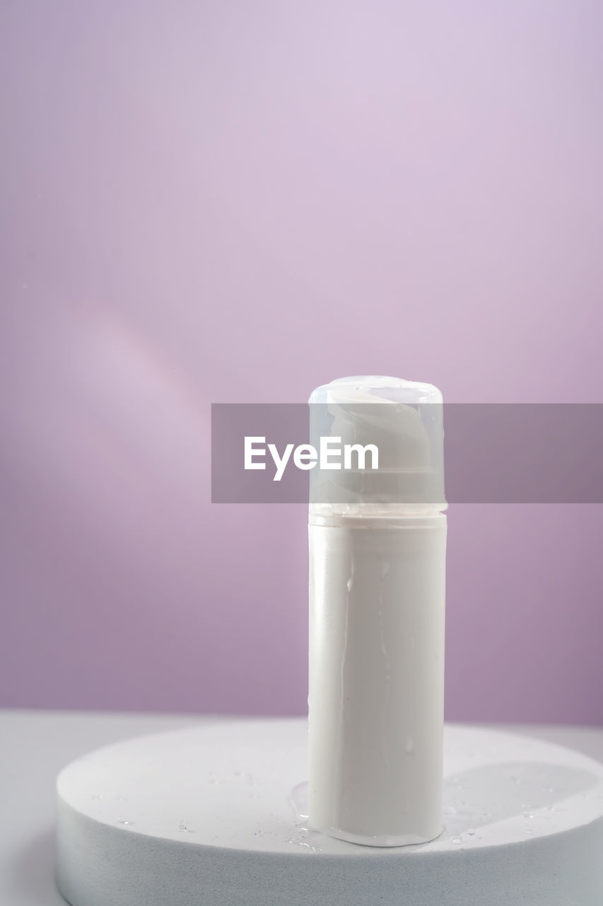 Cosmetic bottle with water splashes on a purple background.