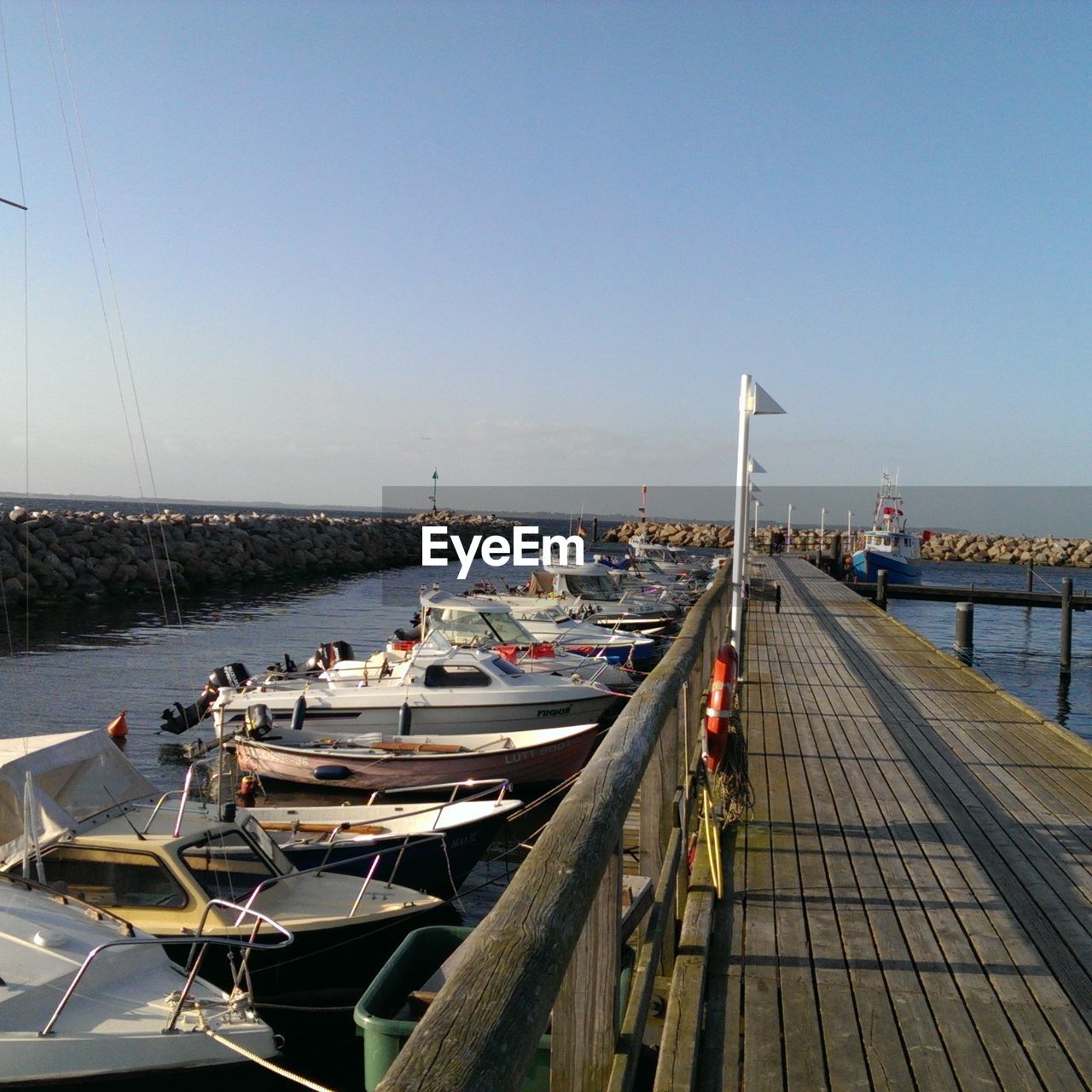 High angle view of pier by boats moored in sea against blue sky