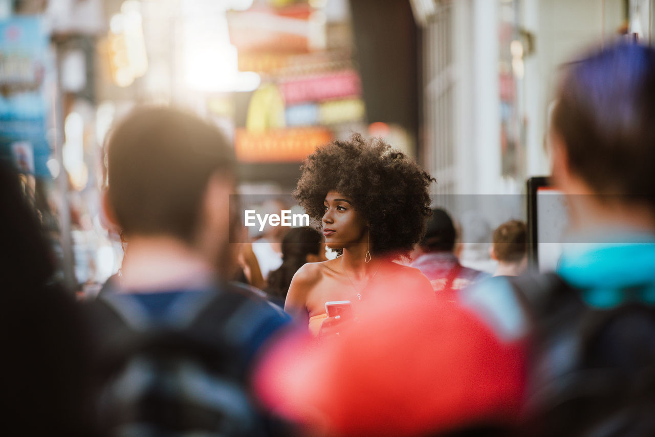 Young woman looking away while holding smart phone on city street