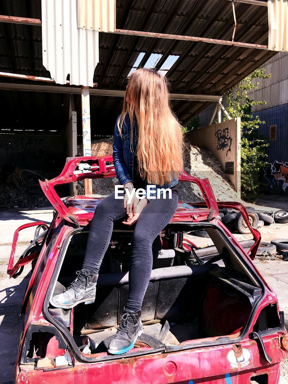 Young woman sitting on abandoned car