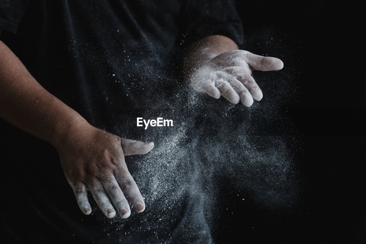 MIDSECTION OF PERSON HOLDING HANDS OVER BLACK BACKGROUND