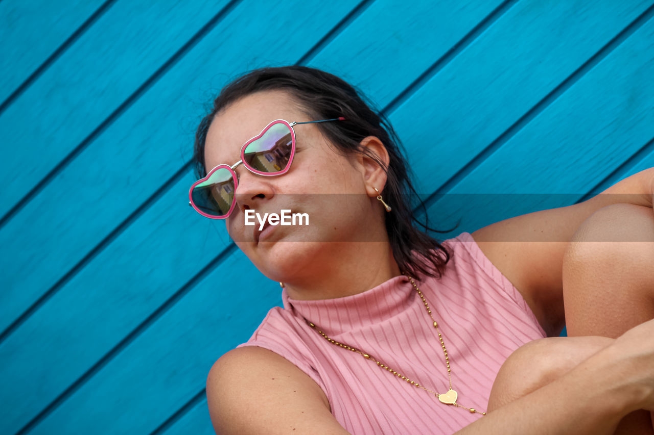 Portrait of young woman wearing sunglasses against wooden background 