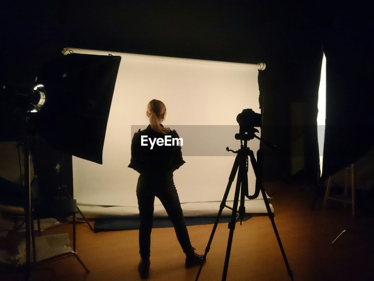 Full length rear view of woman standing by tripod in studio