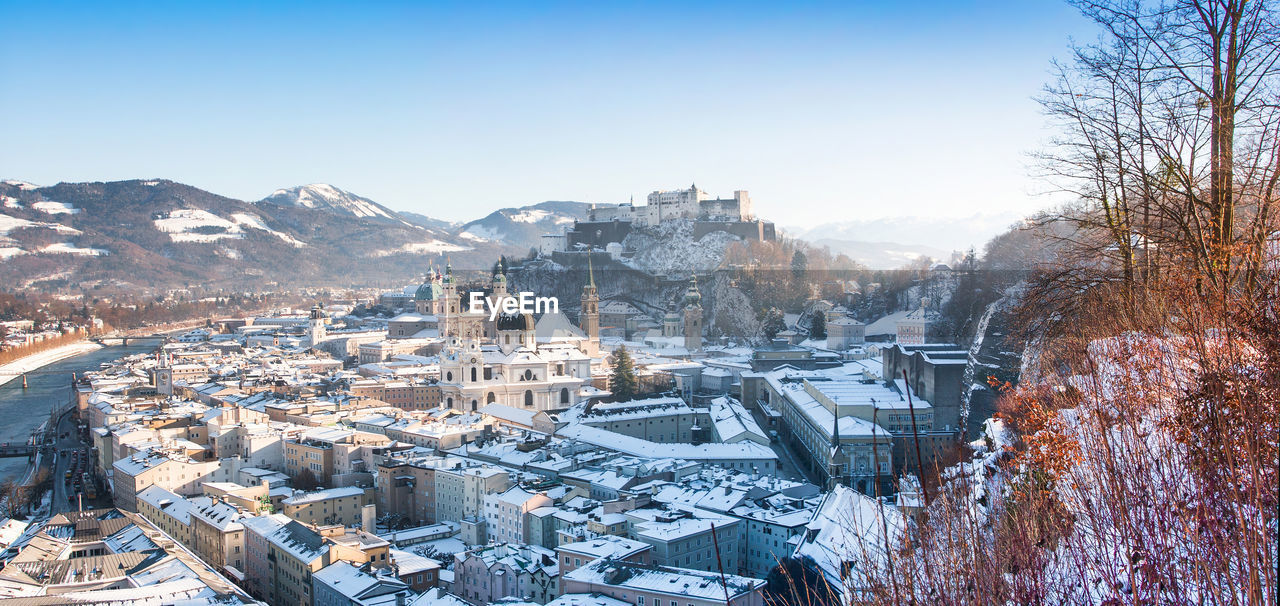 Snow covered townscape by river against clear sky