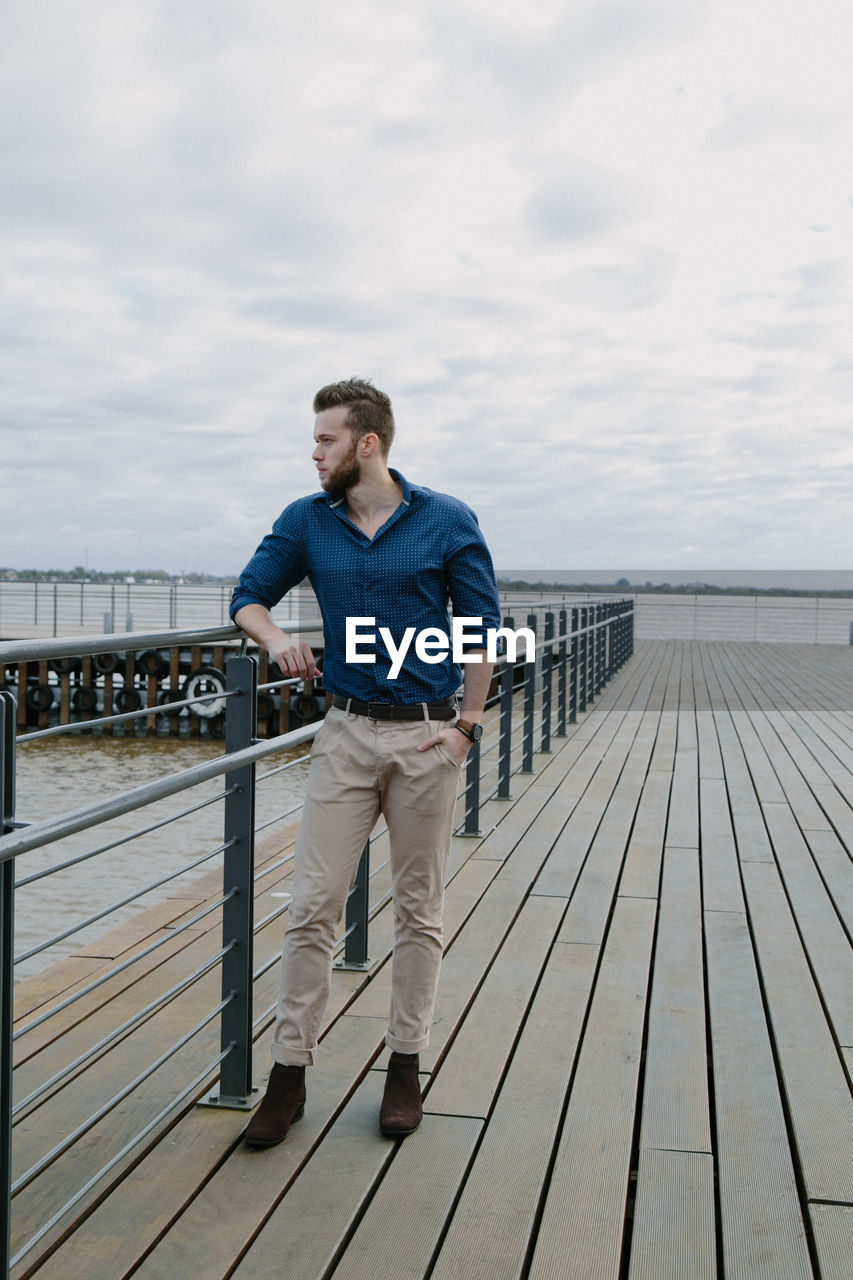 Young man standing on pier against sky