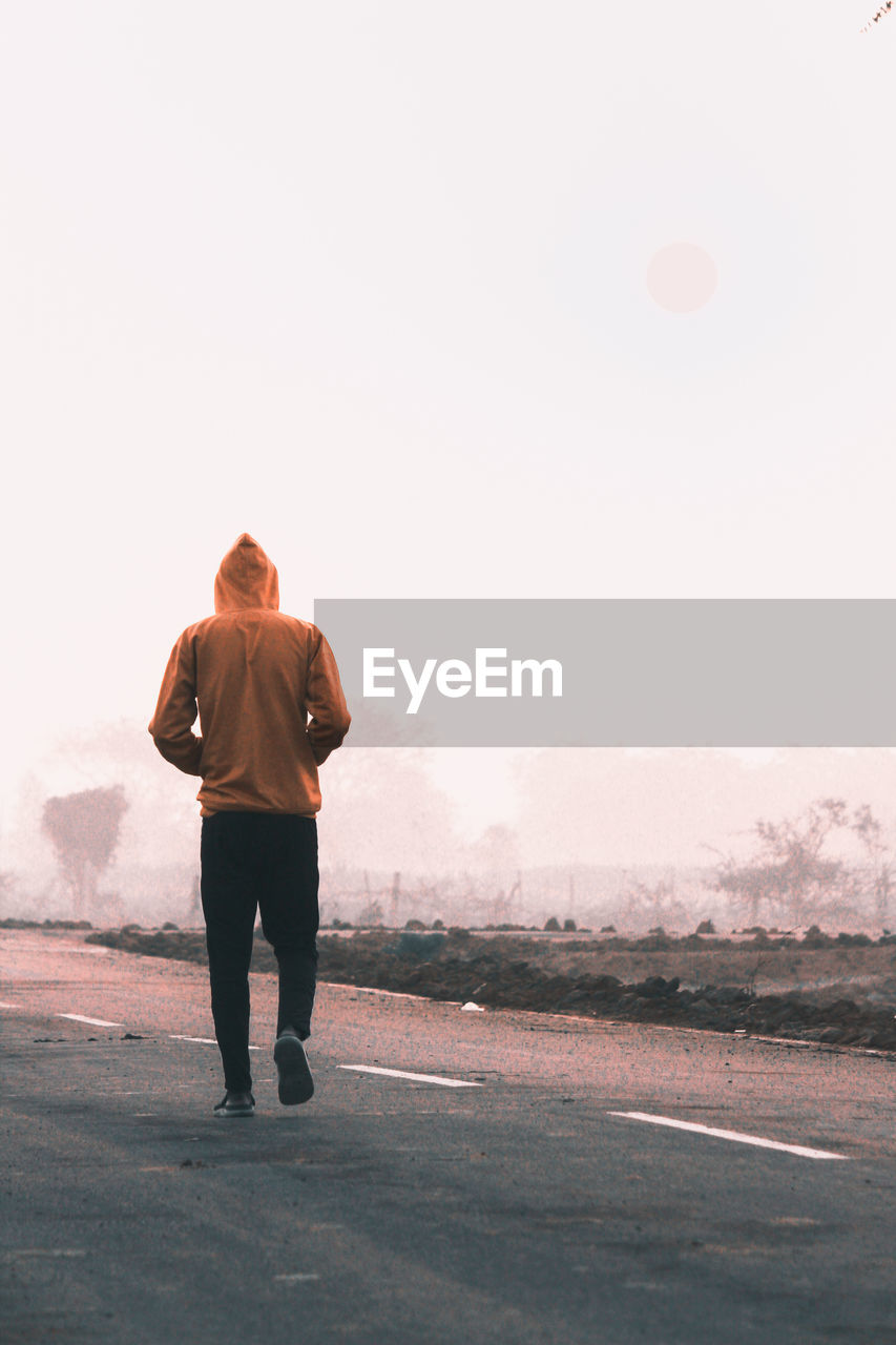 Rear view of man walking on road against sky