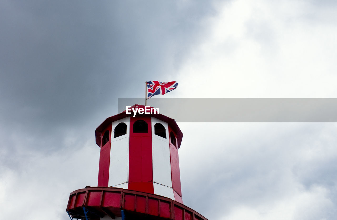 Looking up at a helter skelter with a union jack flag flying at the top against a dark cloudy sky