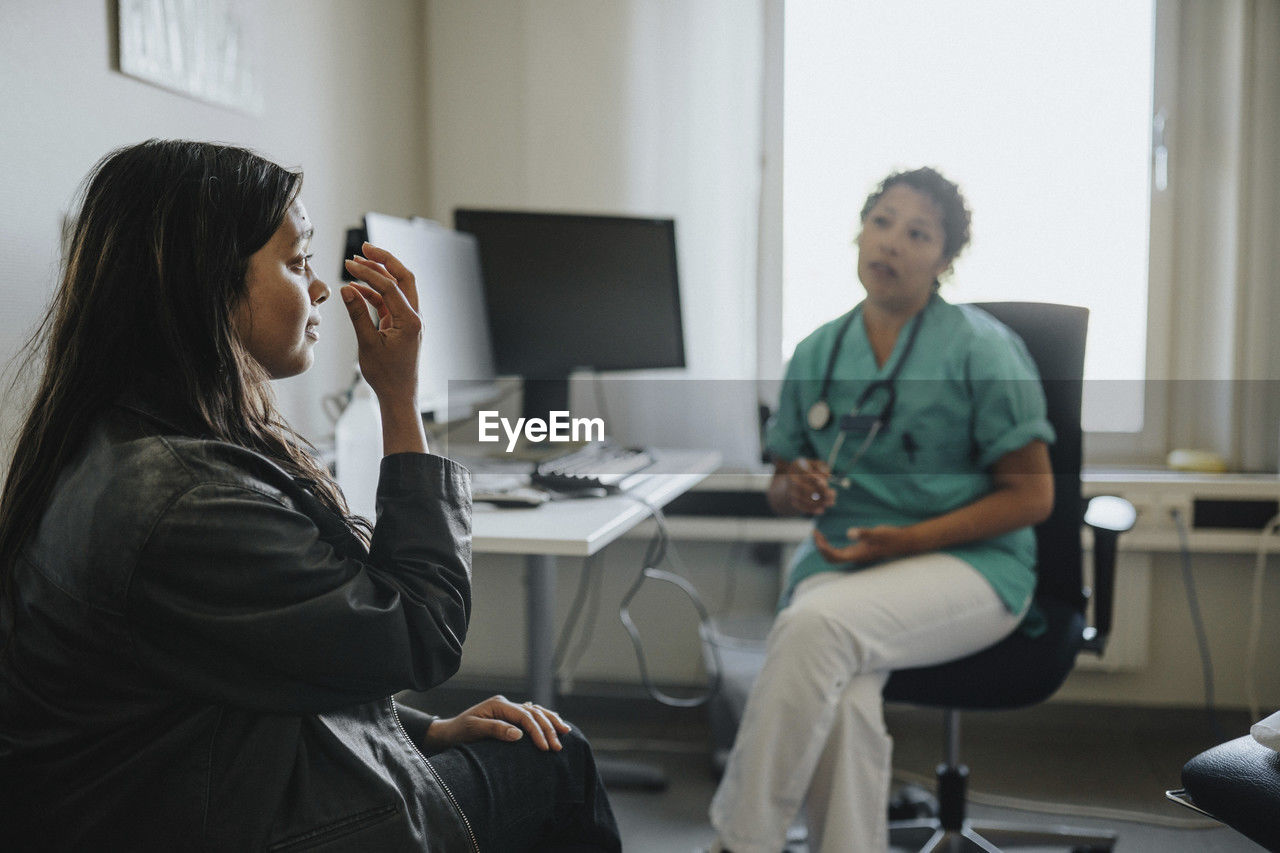 Young woman explaining female physician while sitting in clinic