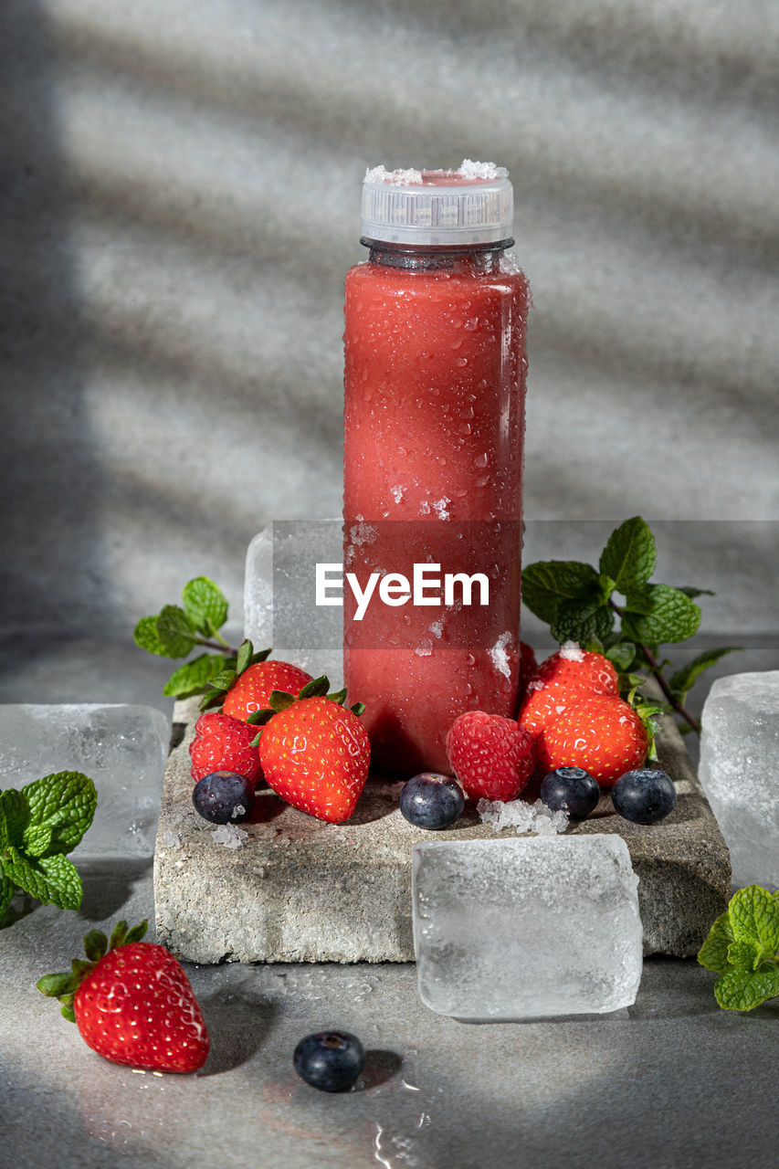 Ice-cold bottle of strawberry smoothie on dark background with copy space. vertical format.