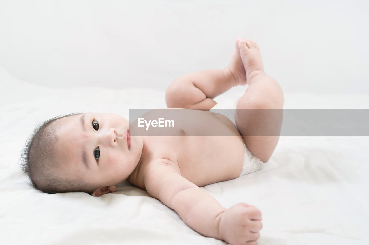 Portrait of a cute little baby boy in diaper lying on white bed.the care for the baby.