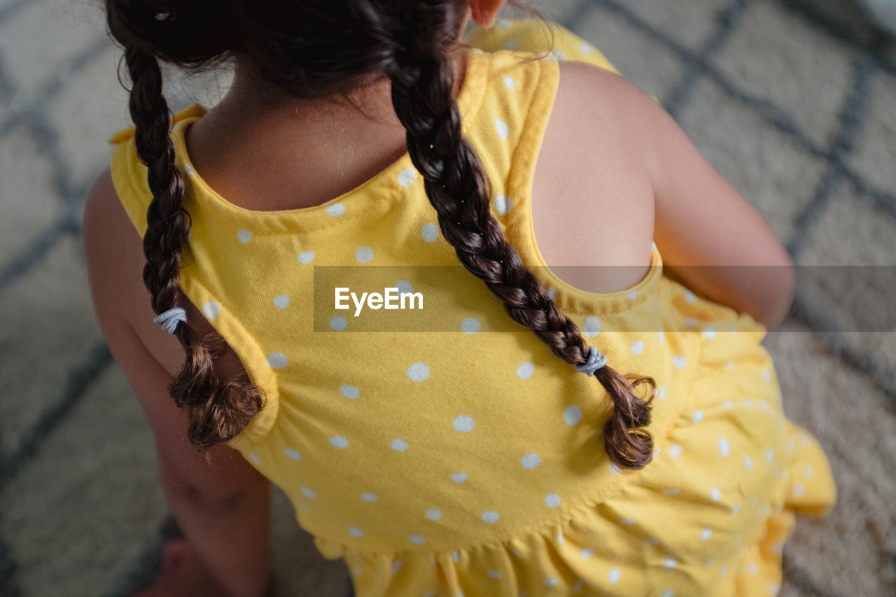 Little girl with braids in yellow dress from behind