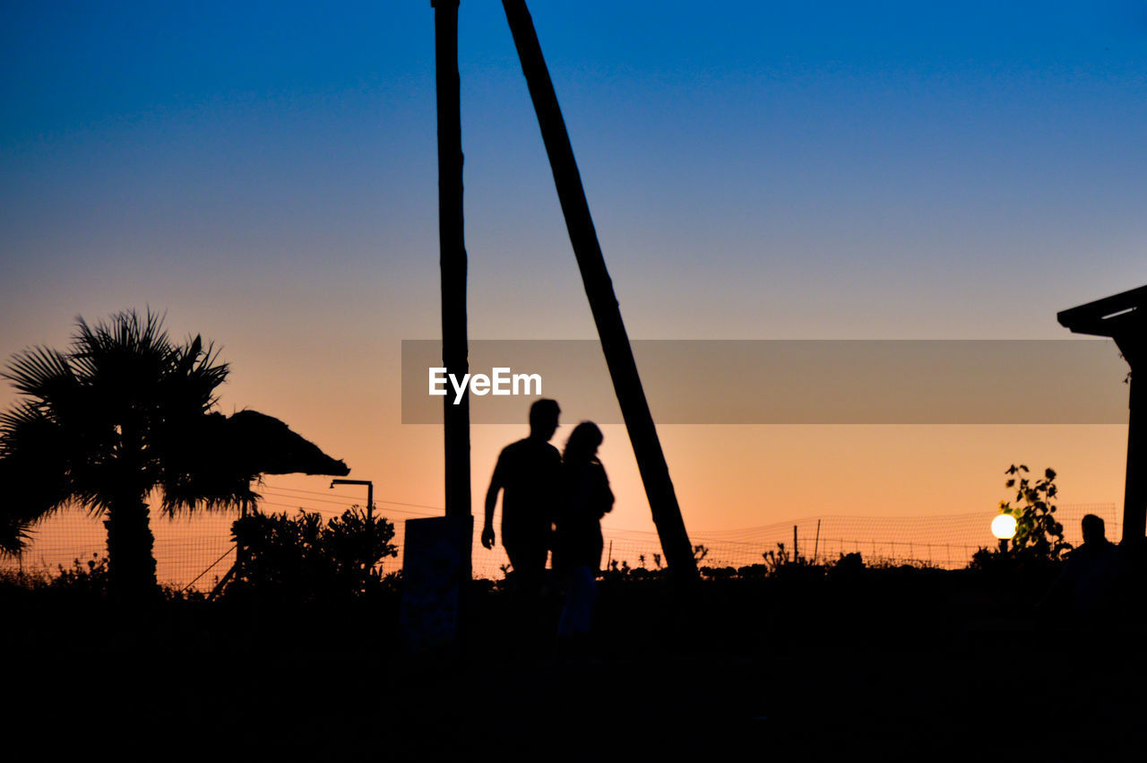 Silhouette man and woman walking against clear sky at sunset