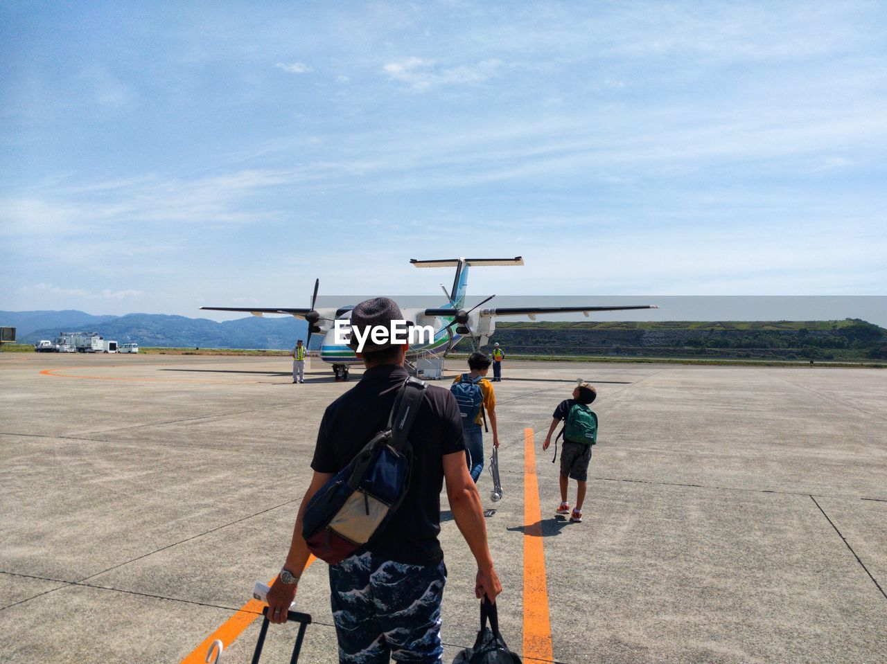 REAR VIEW OF MAN STANDING ON AIRPLANE AT AIRPORT