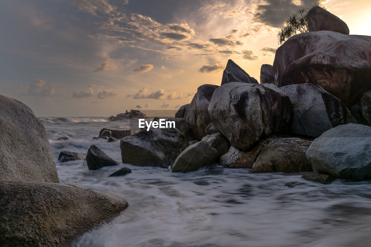 Rocks on beach against sky during sunset