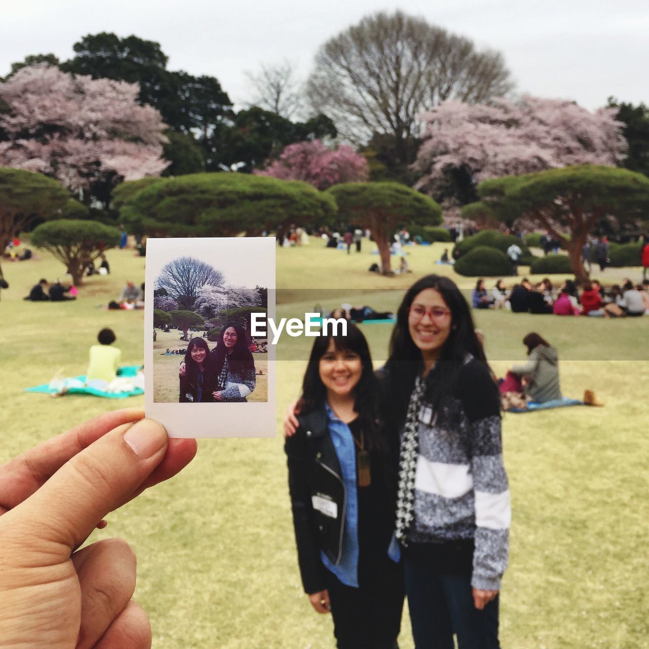 Cropped image of hand holding polaroid against mother and daughter at park