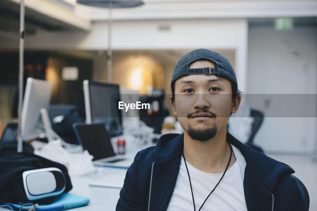 Portrait of confident computer programmer wearing cap in office