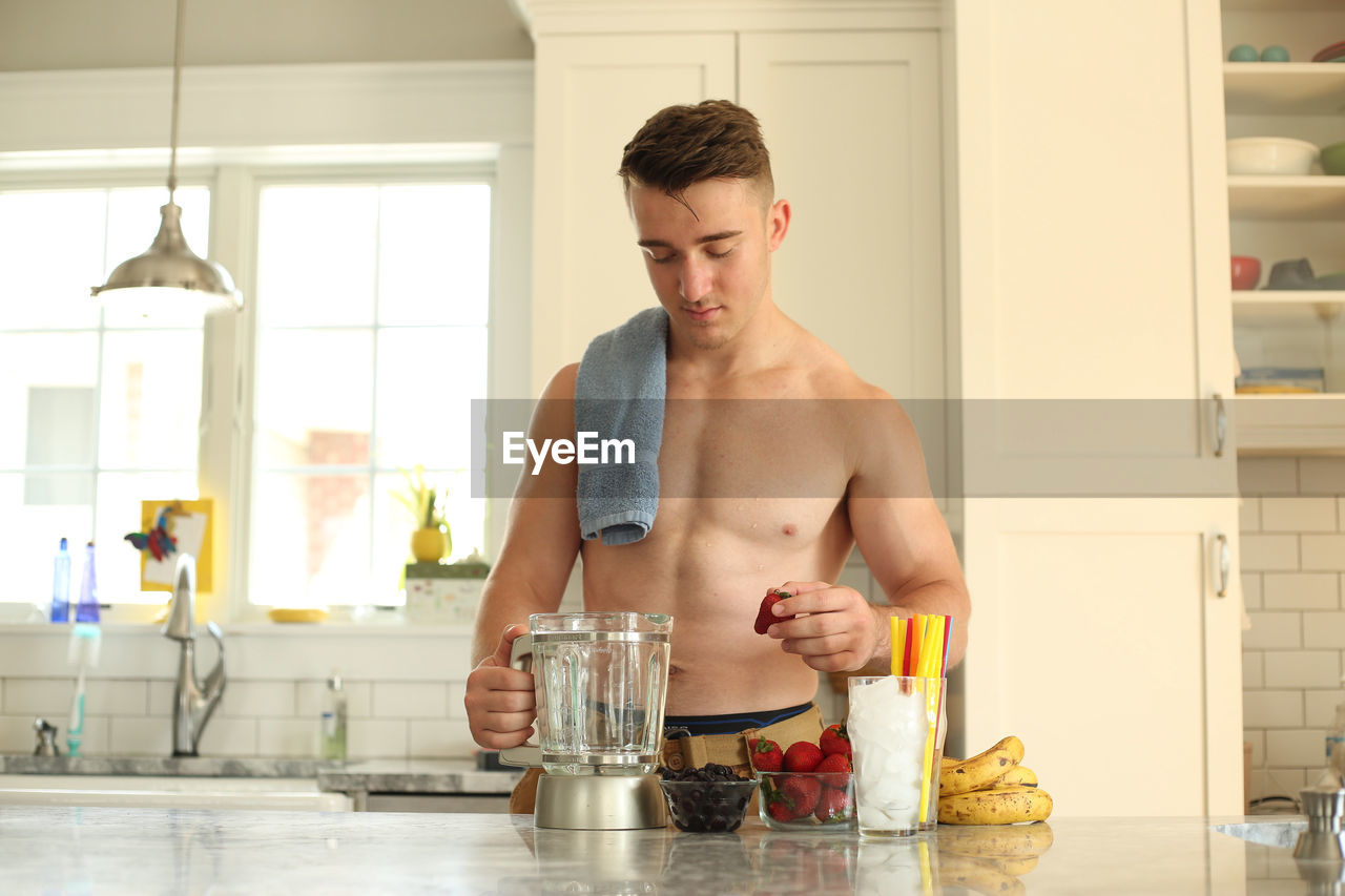 Shirtless teenage boy preparing juice in kitchen at home