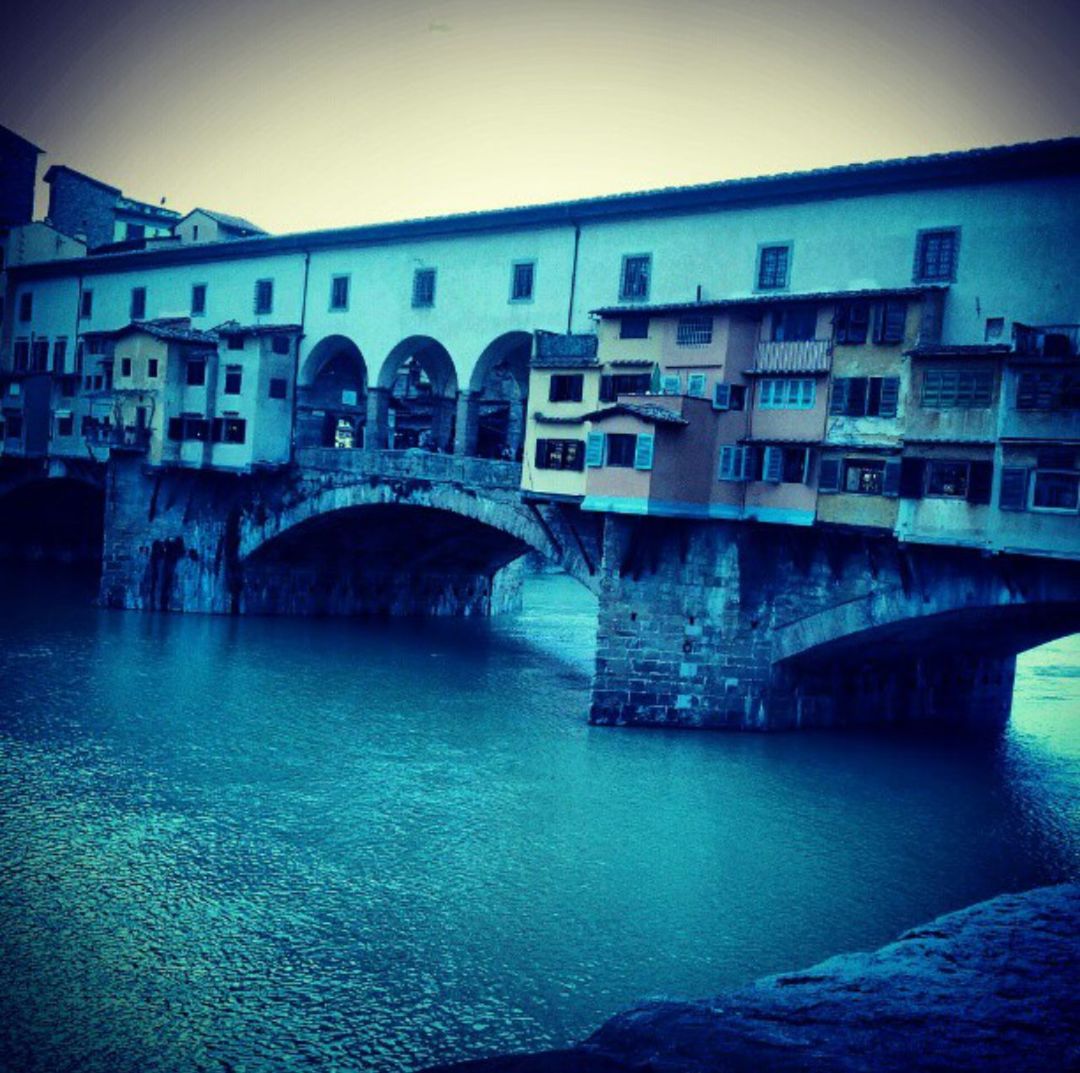 BRIDGE OVER RIVER WITH BUILDINGS IN BACKGROUND