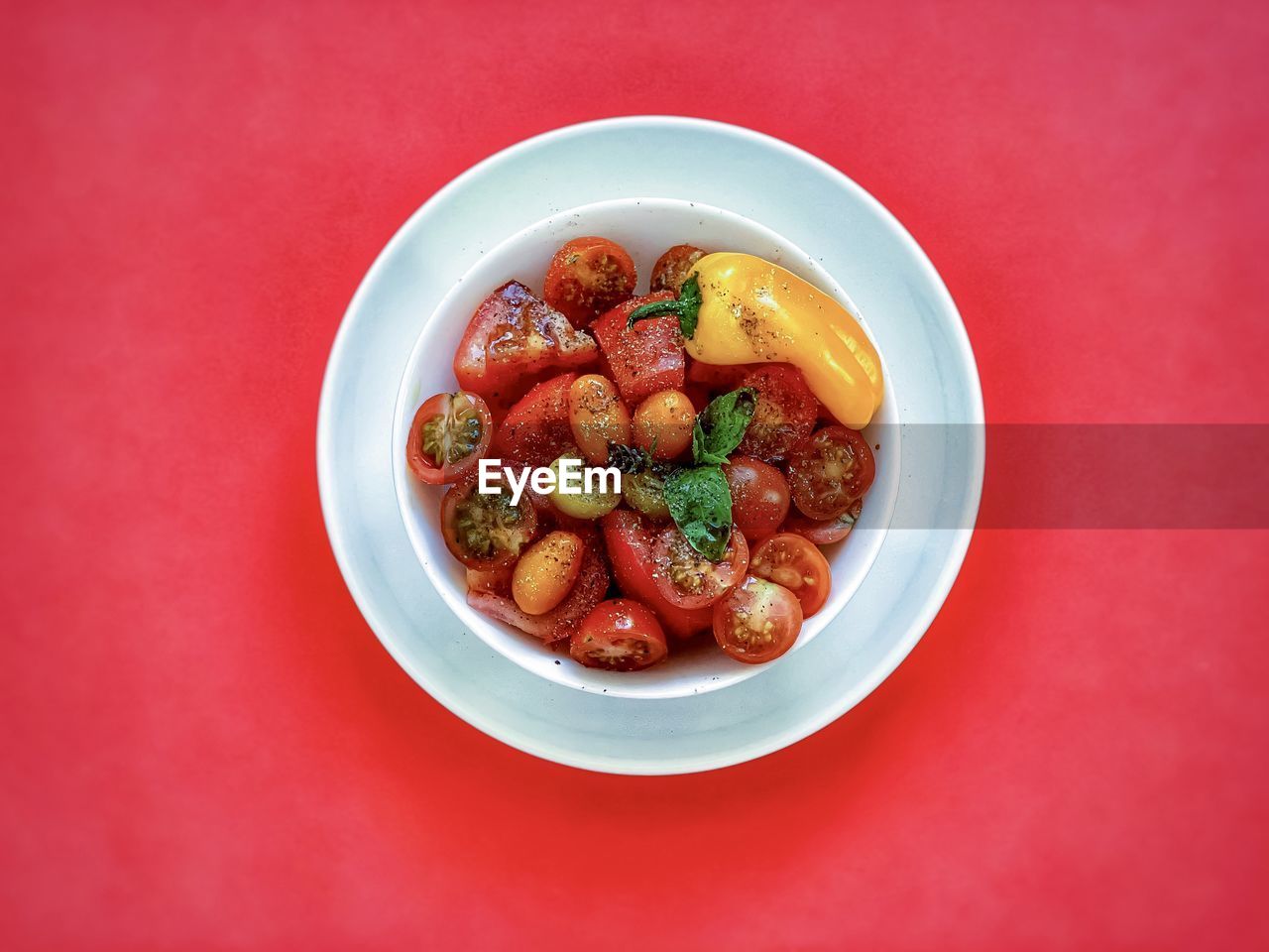 High angle view of sliced tomatoes with balsamic vinaigrette in white plate on red background.