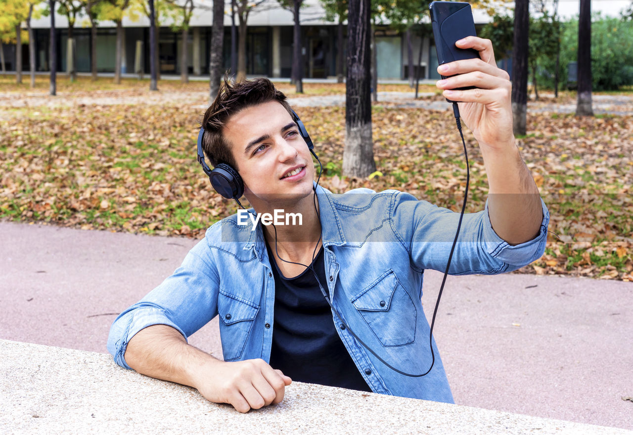 Man listening music while taking selfie in city