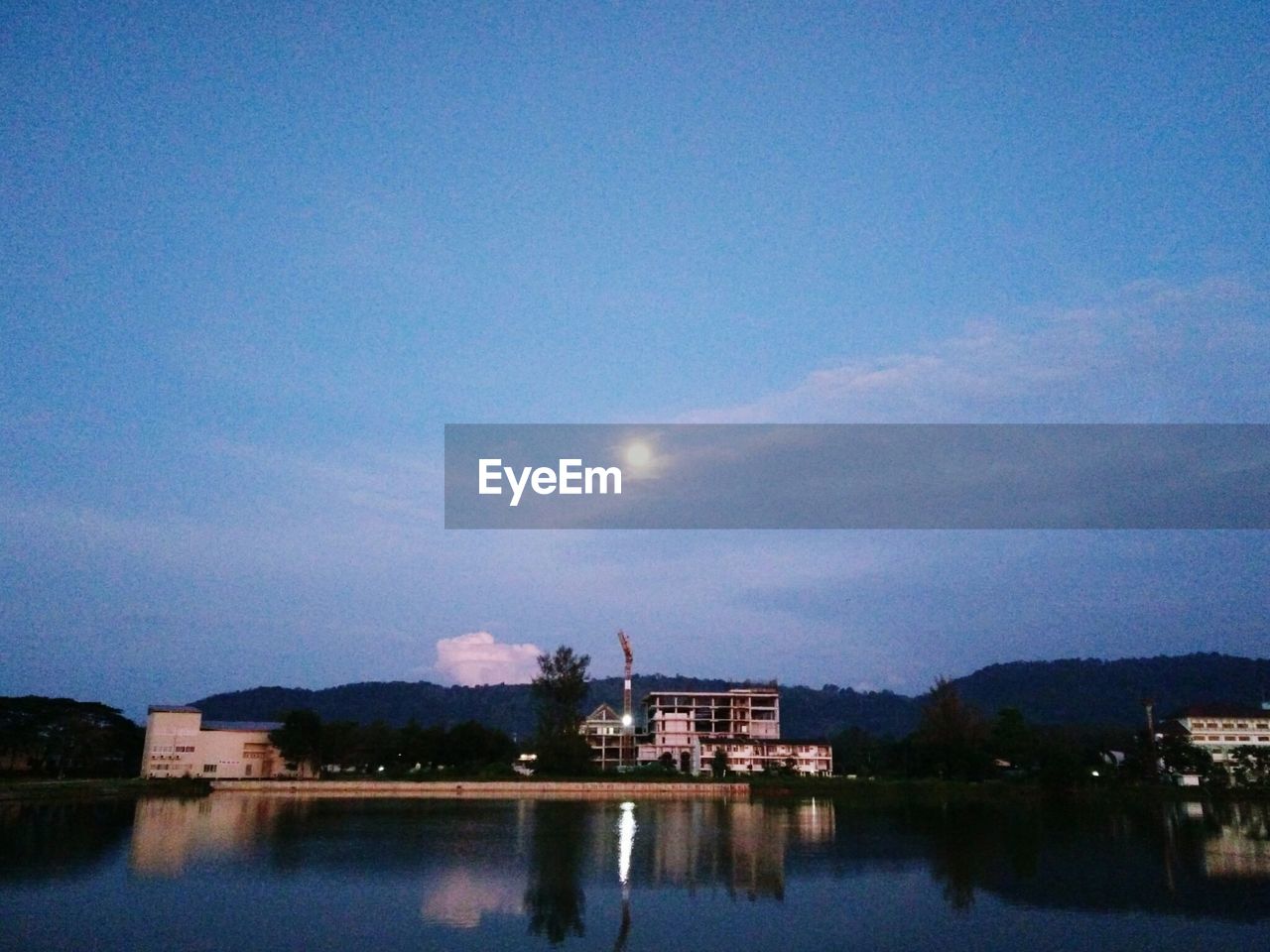 REFLECTION OF ILLUMINATED BUILDINGS IN LAKE AGAINST SKY IN CITY